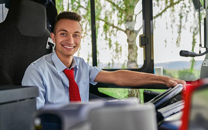 Ein Auszubildender zum Busfahrer sitzt in Unternehmensbekleidung am Steuer eines Busses